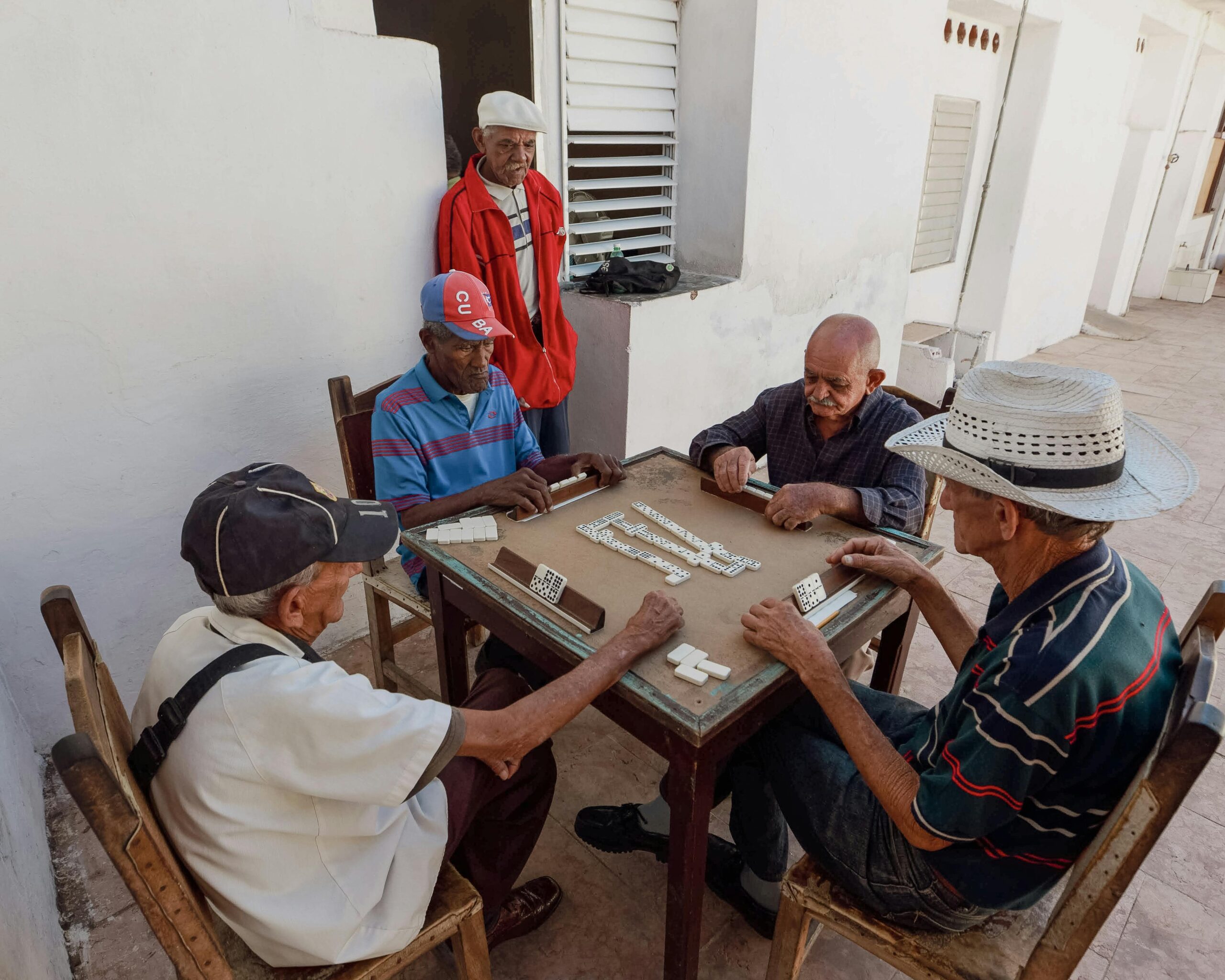 Home A group of elderly men playing dominoes outdoors, showcasing friendship and leisure in retirement.